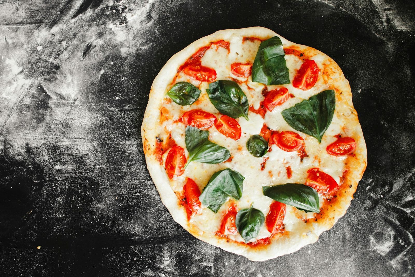 Pizza margherita con pomodorini e basilico su un piano infarinato